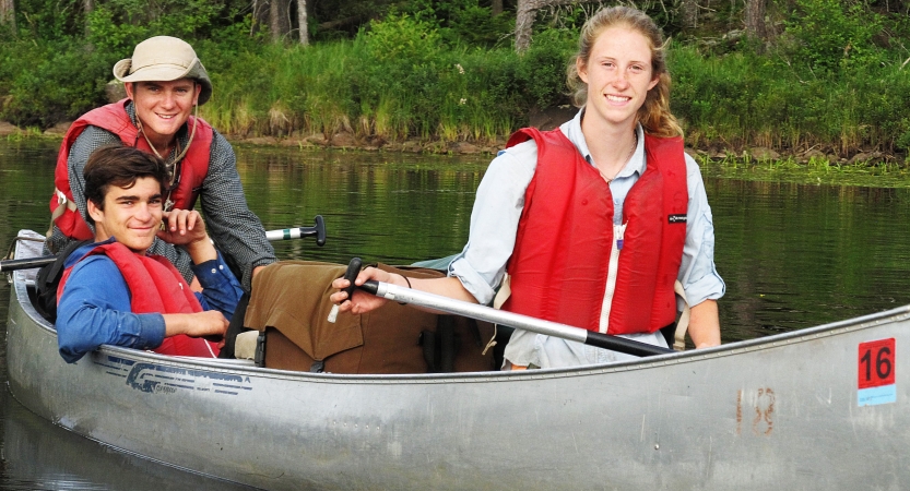 Three people in a canoe smile at the camera.