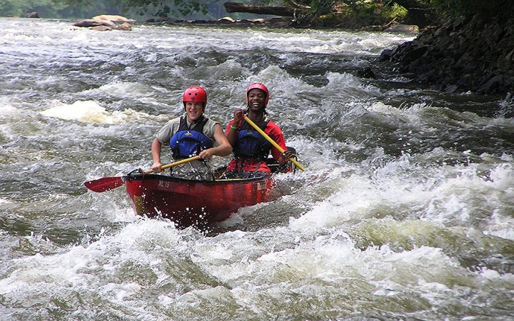 two students wearing safety gear navigate a canoe through whitewater in north carolina on an outward bound trip