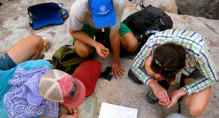 three students examine a map while one of them holds a compass