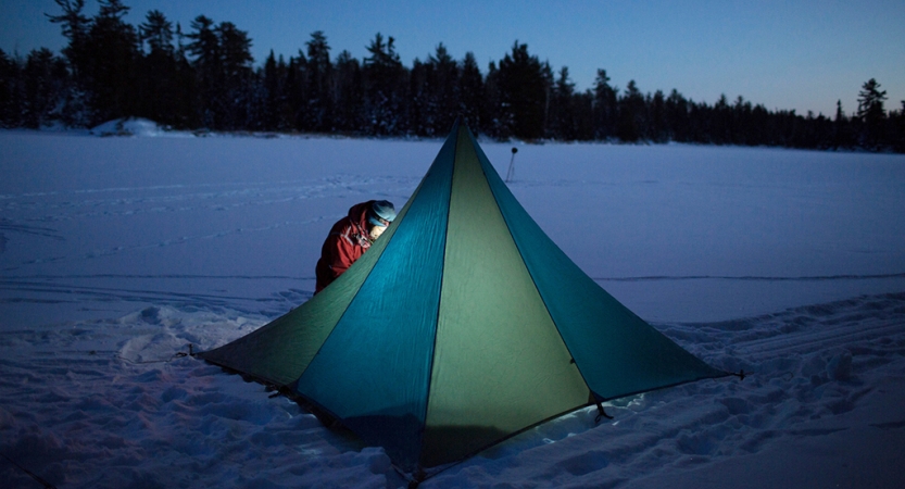 a tent resting on a snowy landscape is illuminated by a person's headlamp