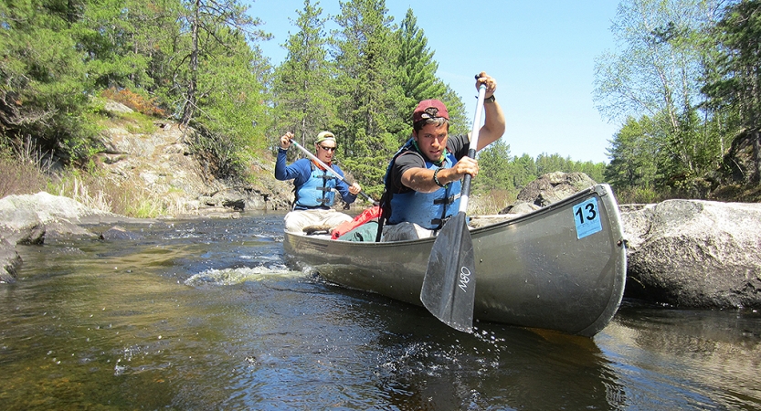 two gap year students paddle a canoe  between rocks